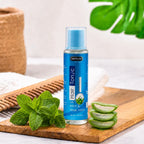 Hair tonic with mint & aloe vera on wooden tray, fresh herbs beside bottle for natural hair care
